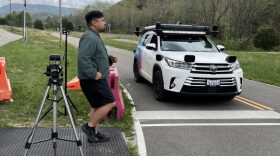 A man faces a crosswalk as a white car approaches from his left. 