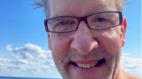 Close-up of a man next to a large body of water; man looks as though he just got done swimming