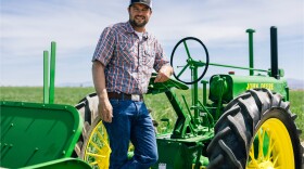 Colby Frey leans on a green John Deere tractor.