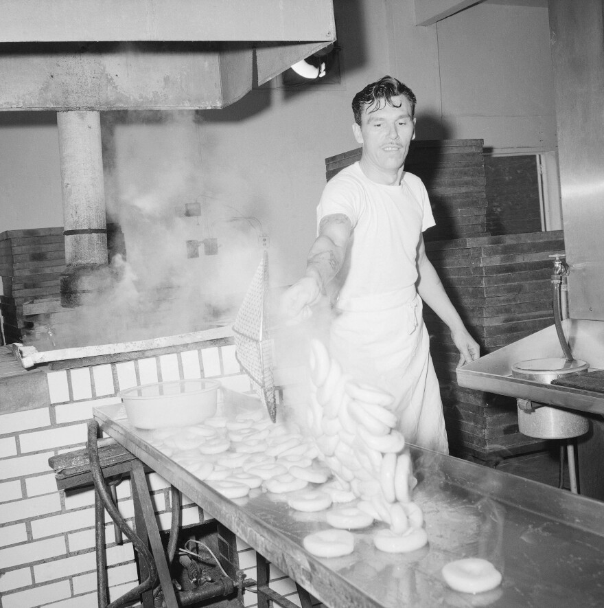 Steaming-hot bagels are scooped out of the water in which they were boiled and dumped onto a stainless steel drain board at a bagel bakery in Queens, New York City, 1963. Traditionally, bagels were boiled, but bakers who use the modern method skip this step.