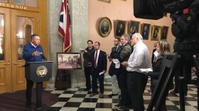 Fresh from a trip to New Hampshire, Gov. John Kasich talks to reporters in front of his ceremonial Statehouse office.