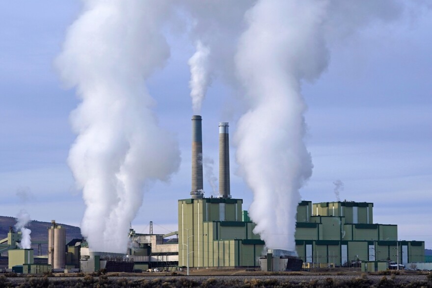 A large power plant with smoke stacks and lows of white smoke