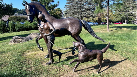Statue of a girl walking a horse alongside a running dog.