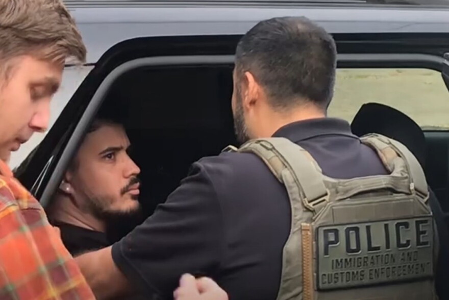Immigration and Customs Enforcement police officer confronting man in back of police vehicle.