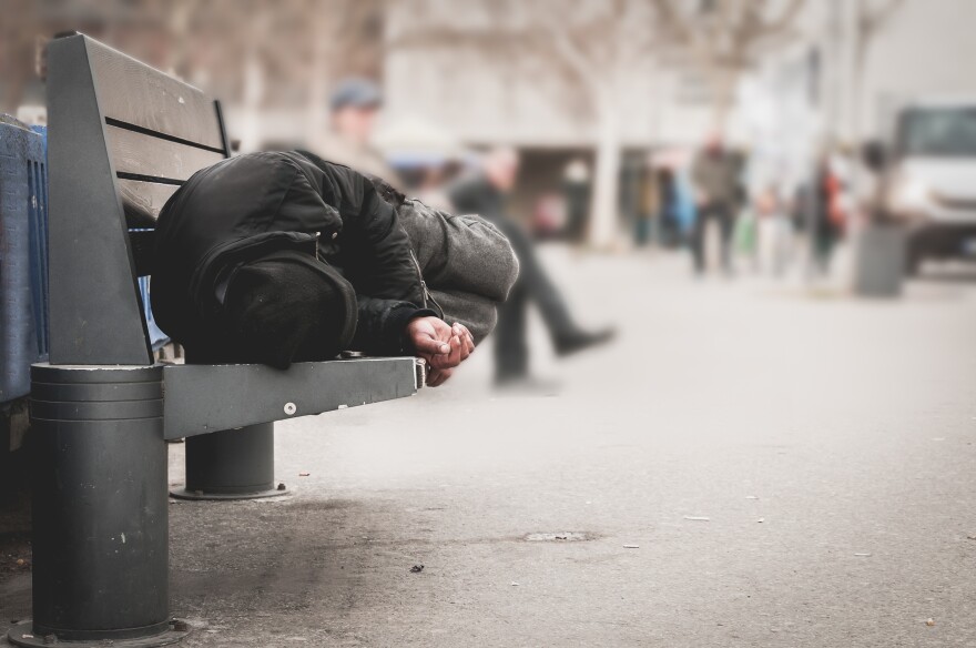 Poor homeless man or refugee sleeping on the wooden bench on the