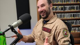 A man in a tan ghostbusters outfit sitting in front of a microphone