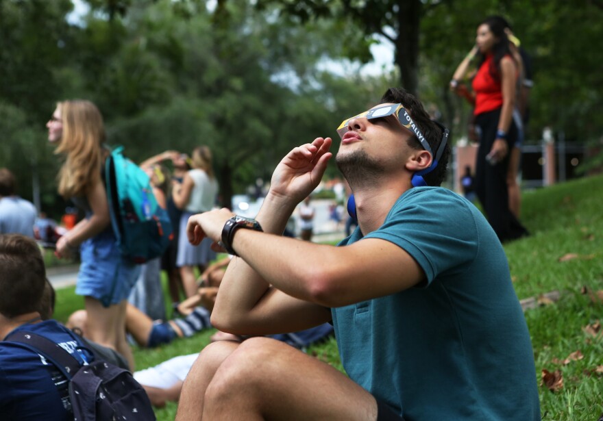 John-Paul Vitucci, a 19-year- old UF mechanical engineering sophomore, looks at the sun through borrowed eclipse glasses. While he said he was disappointed that the clouds sometimes blocked the view, he said, “It’s pretty unique.” (Emma Green/WUFT News)