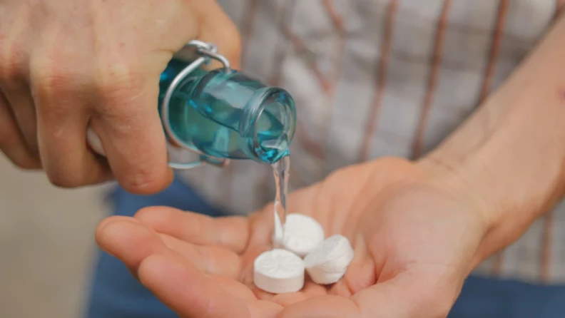 Image of hand cupping 3 dry towelettes while the other hand pour water over them from a glass bottle