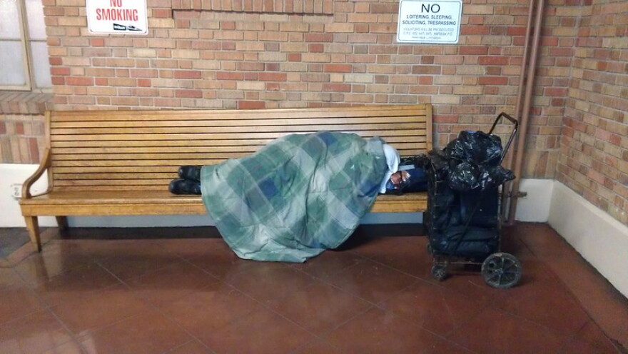 A homeless person sleeps on a wooden bench inside San Jose's Diridon station.