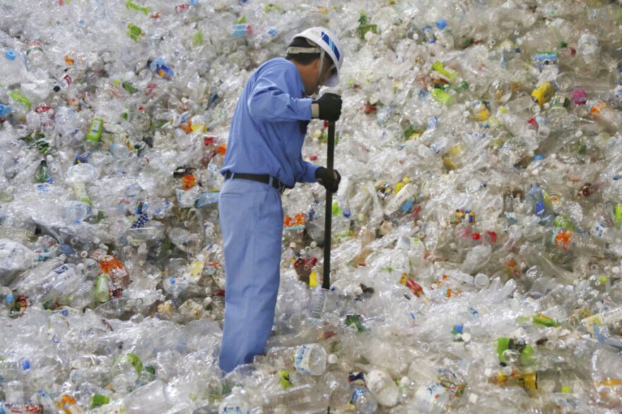 A recycling plant worker sorts enormous piles of plastic bottles.