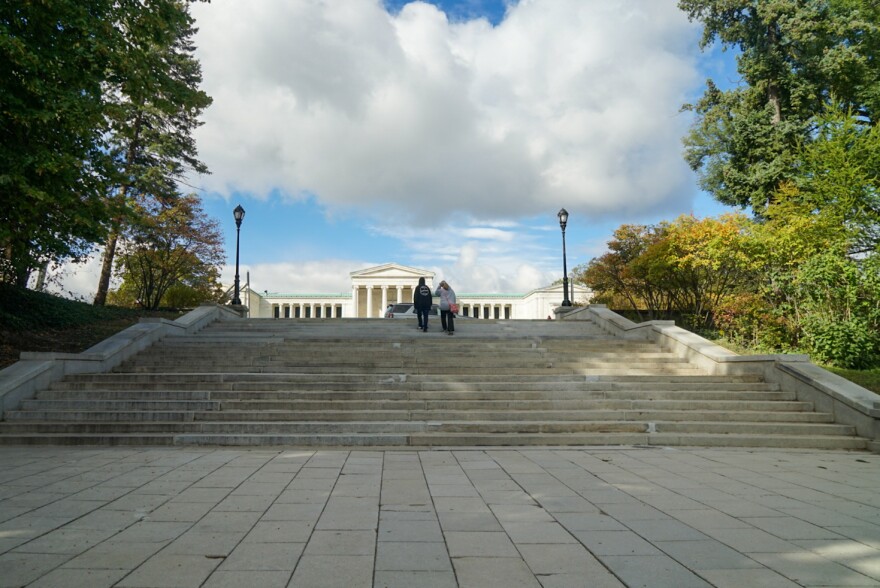 A forward-facing image of the Grand Staircase at Delaware Park. Two people walk up the stairs towards the Albright Knox Gallery that stands in the background.