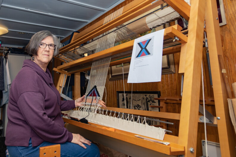 Linda Morton-Kiethley sits at her largest loom, a tapestry loom, in her home studio in Melba, ID. She’s weaving a pattern to be installed on a handmade leather purse, a bright triangle of yarn before her, in red, blue, green and gray.