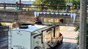 An RV trapped under the Pennsylvania Avenue bridge because of its height. Cutouts of sharp teeth and googly eyes have been placed above on the bridge