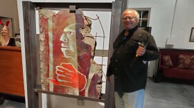 A man with graying hair smiles next to a piece of concrete that is painted with a red hand and inquisitive man's profile