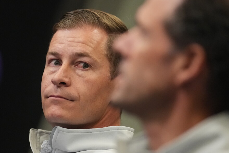 Walker Monfort, back, president of the Colorado Rockies, listens as Paul DePodesta speaks during a press conference.