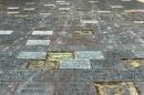 A close-up picture shows a paved walkway of memorial bricks. There are several empty spots where bricks have been dug up. 