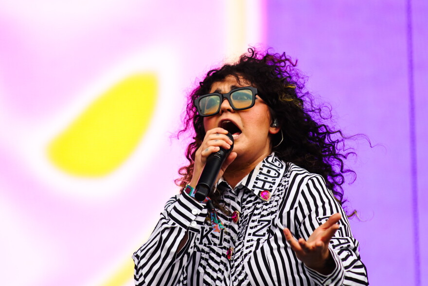Remi Wolf sings onstage with a purple background behind her. 