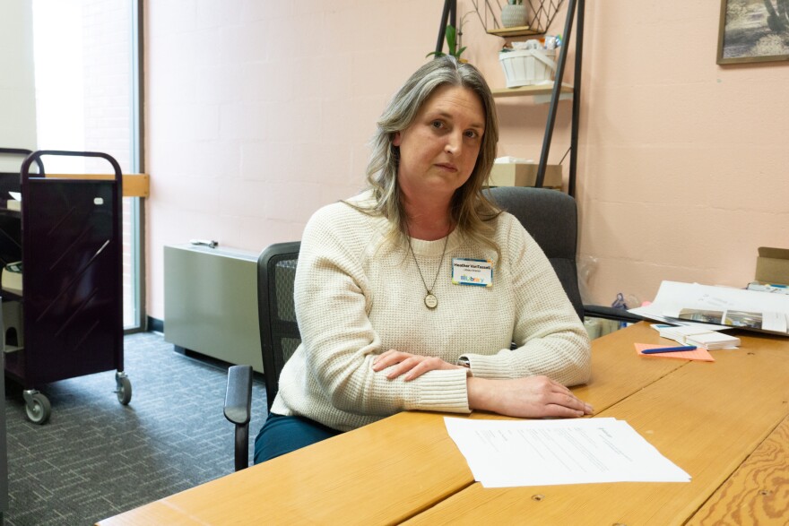 A woman in a white sweater looks at the camera while sitting behind a desk