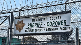 A sign reading Mendocino County Sheriff Coroner Maximum Security Detention Facility on a chain link fence beneath rolls of razor wire.
