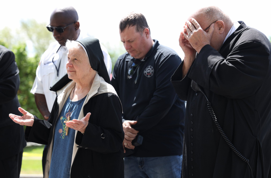 At right, Paul D. Seil, chaplain of the Buffalo Fire Department, covers his face as people pray Tuesday outside the Tops on Jefferson Avenue in Buffalo, the site of a racist mass shooting that left 10 people dead.