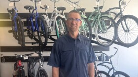 A man in a short-sleeved, blue button-down shirt stands in front of a two-tiered bicycle display.
