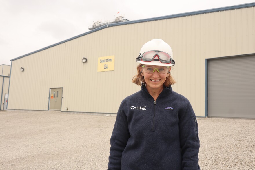 Director of Technology and Sustainability Andrea Vanderhoff wears a hard hat and branded zip-up and stands in front of QORE's separations building.
