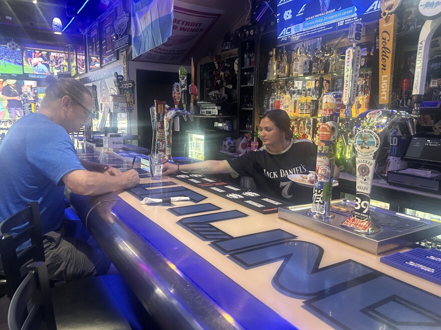 A bartender at The Blue Line is servicing a customer during lunchtime. The Bar also operates as a restaurant where customers frequent during lunch. 