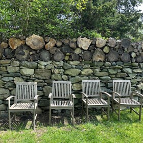 A row of chairs in front of a stone wall with logs on top of it.