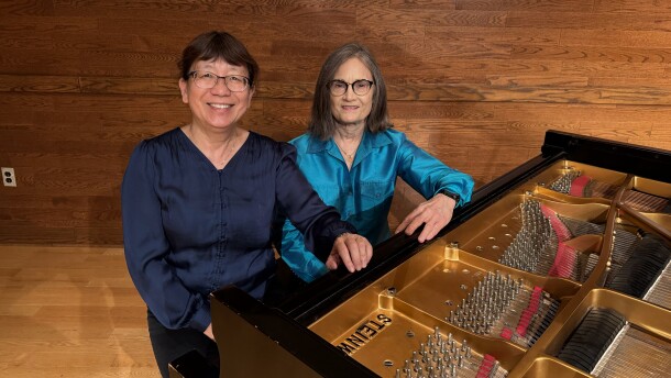 Two women sit at a piano, pictured from above