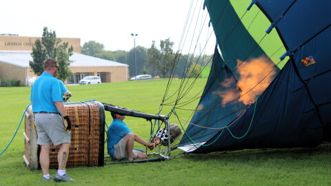 Balloon meister Austin Hopp, crouching, fires up large propane tanks to upright his hot air balloon. He's among 19 pilots planning to fly over the City of Lincoln this weekend as part of its signature Balloons Over 66 festival.