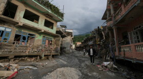 People walk along a street lined with damaged structures after flash flooding in the Devighat area of Nuwakot district in Nepal on Friday, Aug. 28, 2026.