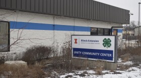 A white building with a large blue and white sign sitting in front of it that reads, "Unity Community Center."