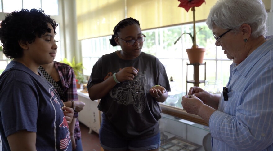 In the documentary, Her Voice Media fellows Satara Masengarb and Tamiah Rogers examine vintage pearl buttons made from upper Mississippi River clamshells with Merredith Peterson, former president of the Rock Island County Historical Society.