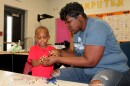 Head Start teaching assistant Shavonda Willis helps Jemez Jackson Harris IV close a bracelet he made to practice patterns June 23, 2017.