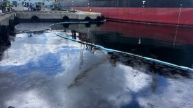 Oil spill in water between a dock and a large ship. 