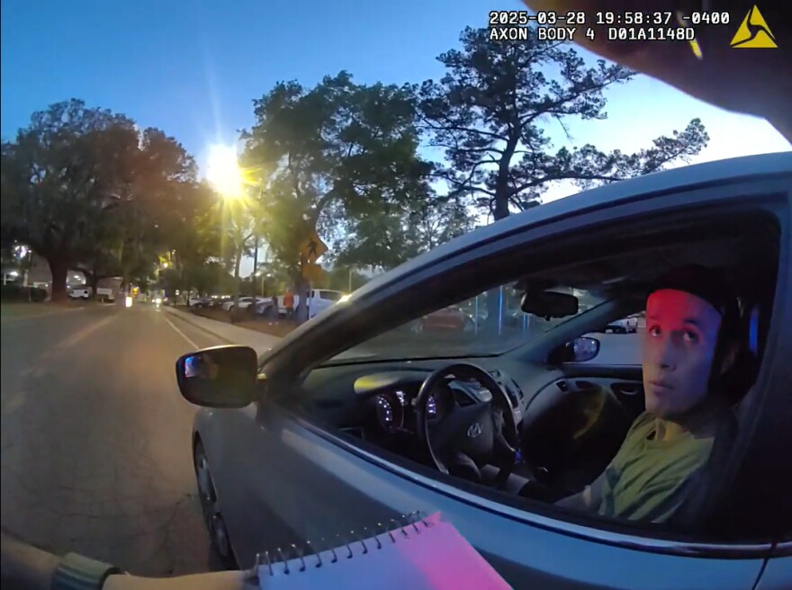 A man sitting in a car looking up at a police officer who's wearing bodycam video