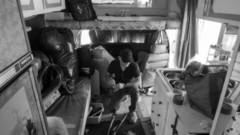 Miguel Mercado, a man in dark clothing and a baseball cap, packs up his belongings. He's in the RV where he lived until March 2026, when city staff towed the RV.
