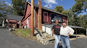 two women stand on a black driveway in front of a red barn that has a "Dexter Cider Mill" sign on it