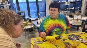 Two women carefully work with gold leaf and a table with an entire collage spread out.