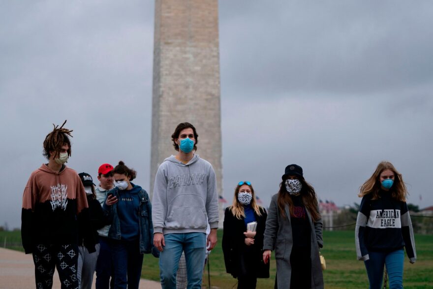 A group of young people wear protective masks as they walk near the Washington Monument in Washington, D.C.