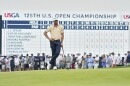 A man with a golf club stands on a field by a crowd.