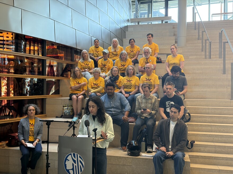 A group of activists stand behind a podium for a press conference on the steps inside Seattle City Hall. 