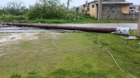 A power pole snapped from its base lies across a road in Rota following the landfall of Typhoon Bavi, with downed lines and a damaged transformer visible amid storm debris.