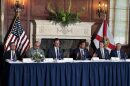 A panel of politicians sitting at a blue table with flags behind them 