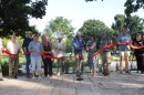 A group of people stand behind a red ribbon with a big pair of scissors, cutting the ribbon. 