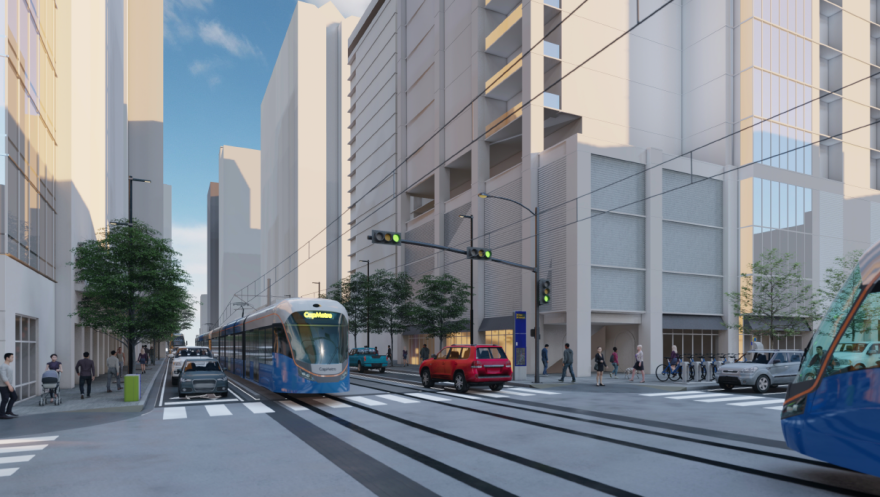 An illustration showing a light-rail vehicle running at street level at East 3rd Street and San Jacinto Boulevard. The train is blue with a white roof and orange highlighting. The destination sign says "CapMetro." Gantry lines are running overhead.