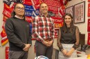 three people smile in front of soccer scarves