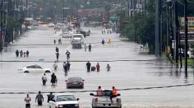 People walk through the flooded waters of Telephone Rd. in Houston on Aug. 27, 2017 as the U.S. fourth city city battles with tropical storm Harvey and resulting floods. (Photo by Thomas Shea/AFP via Getty Images)