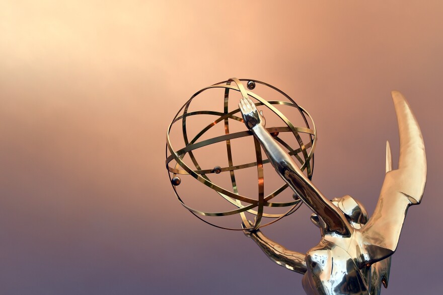 A gold Emmy statue is pictured in front of a pink and purple background.