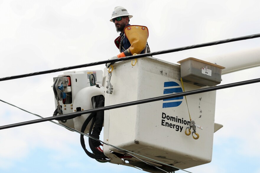 FILE - A Dominion Energy lineman lifts himself up to work on a power line